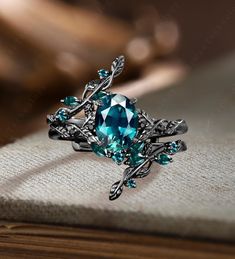 a ring with blue stones and leaves on it sitting on top of a cloth covered table