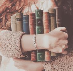 a woman is holding several books in her hands while wearing a bracelet with the word love written on it