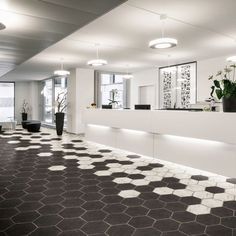 an office lobby with black and white tiles on the floor, potted plants in vases