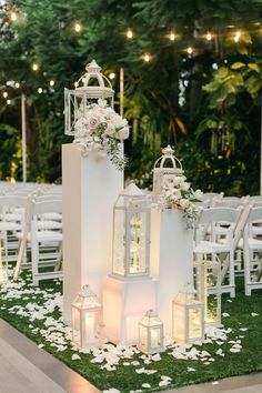 an outdoor ceremony setup with lanterns and flowers on the grass, candles in front of them