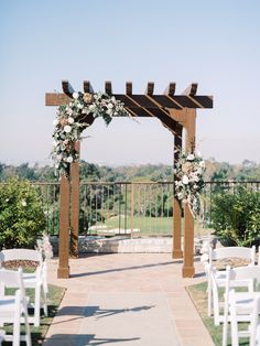 an outdoor ceremony setup with white chairs and flowers on the arbors at this wedding venue