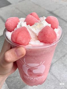 a person holding up a pink drink with marshmallows on top