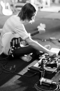 a man sitting on the ground with his guitar in front of him and other electronic equipment around him