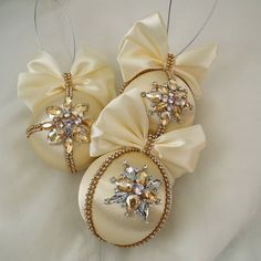 three ornaments with bows on them sitting on a white cloth covered tablecloth, one is gold and the other is ivory