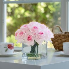 a vase with pink roses in it sitting on a table next to a cup and saucer