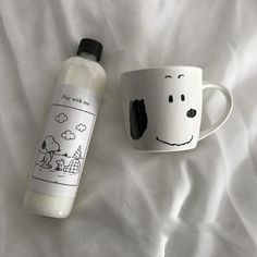 a coffee cup next to a ceramic mug with a drawing on it, sitting on a bed