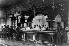 an old black and white photo of people standing in front of a bar with men sitting at it