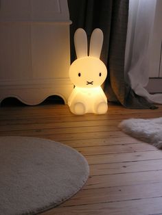 a white rabbit lamp sitting on top of a wooden floor next to a rug and window