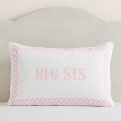 a pink and white pillow with the word big sis on it sitting on a bed