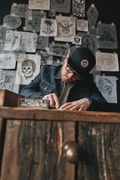 a man sitting at a wooden table using a cell phone and wearing a black hat