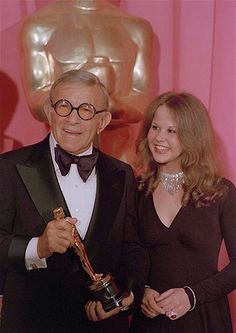 an older man and young woman standing next to each other in front of a pink wall