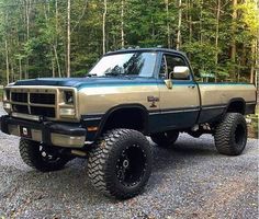 a brown and black truck parked on top of a gravel covered road in front of trees