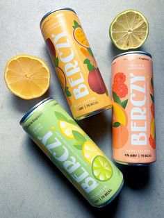 three cans of peach lemonade and two oranges on a gray surface with one cut in half