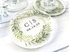 two personalized glass coasters with greenery on the bottom and one for each