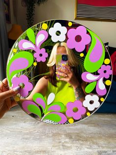 a woman taking a selfie in front of a mirror with flowers painted on it