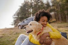 a woman is sitting on the ground with her dog and smiling at the camera,