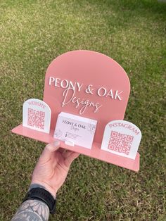 a person holding up a sign that says peony and oak designs in front of some grass