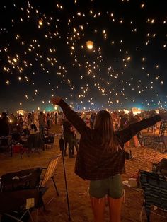 a woman standing in the sand with her arms up and lights flying above her head