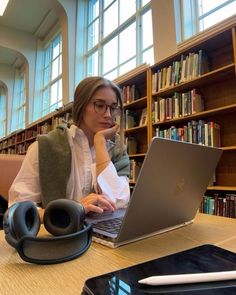 a woman sitting in front of a laptop computer on top of a wooden table next to a book shelf