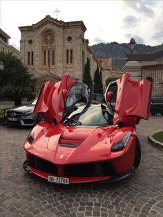 a red sports car parked in front of a church with its doors open on a cobblestone driveway