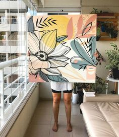 a woman standing in front of a window holding up a large flower painting on the wall