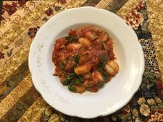 a white bowl filled with pasta and sauce on top of a floral tablecloth covered place mat