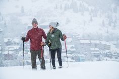 two people standing on top of a snow covered slope with skis in their hands