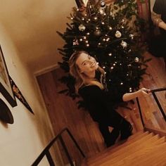 a woman standing on the stairs in front of a christmas tree