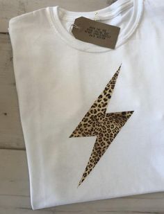 Womens leopard print tshirt. This tshirt come in white or black with a leopard print lightening bolt!If you love the lightening bolt, please also check out our neon pink lightening bolt tshirt here: https://www.etsy.com/uk/listing/813400863...and our popular rose gold lightening bolt tshirt here: https://www.etsy.com/uk/listing/694995048..or if you're a fan of anything leopard print or animal print, check out our 'Kind Is Cool' leopard print tshirt here: https://www.etsy.com/uk/listing/804918595 Cheap Gold Graphic Tee, Preppy Lightning Bolt Shirt, Cheap Gold Graphic Print Shirt, Cheetah Lightning Bolt Shirt, Popular Tshirt Designs, Animal Print Tshirt, Leopard T Shirt, Leopard Print Sweatshirt, Leopard Print Top