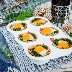 cupcakes with eggs and spinach are on a tray next to pine cones