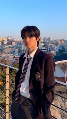 a young man wearing a suit and tie standing on a balcony overlooking a cityscape