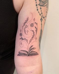 a woman's arm with a book and flowers tattoo on the left side of her arm