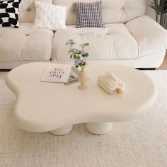 a living room with a white couch, coffee table and potted plant on it