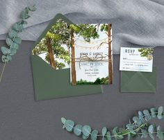 the wedding stationery is set up on top of an envelope and surrounded by greenery