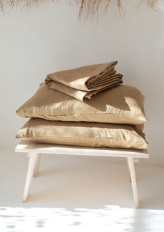 a stack of gold pillows sitting on top of a white table next to a plant