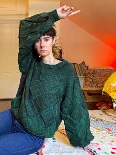 a woman is sitting on the floor with her hands in the air while wearing a green sweater