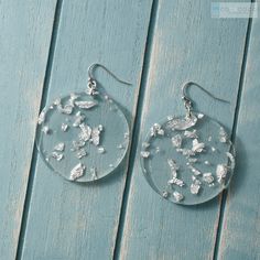 the earrings are made from clear glass with silver flakes on them, sitting on a blue wooden surface