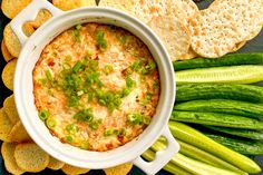 a bowl of dip surrounded by crackers and vegetables