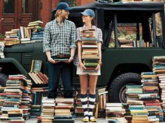 a man and woman standing in front of a pile of books on top of a green truck