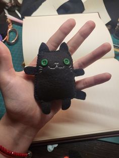 a hand holding a small black cat with green eyes on it's palm, next to an open notebook