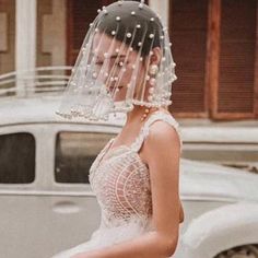 a woman in a wedding dress with a veil on her head standing next to a white car