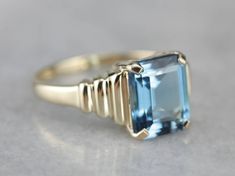 "This beautiful ring has stacked, modern style and a perfectly cut blue topaz center, with tons of life and sparkle and stunning blue hue. Metal: 14K Yellow Gold Gem: Blue Topaz 3.48 Carats Gem Measurements: 7.7 x 9.7 mm, Emerald Cut Ring Size: 7 Marks: \"14K DQ CZ\" Stamped on the inside band SKU #: 52TP199L-P Each piece has been identified and graded by a Graduate Gemologist who has been certified by the Gemological Institute of America (GIA). We have four brick and mortar storefronts in Maine Modern Yellow Gold Blue Topaz Ring, Modern Emerald Cut Topaz Ring, Modern Blue Topaz Ring For Formal Occasions, Modern Blue Topaz Ring For Wedding, Modern Blue Topaz Wedding Ring, Modern Blue Baguette Cut Ring, Modern Topaz Ring With Accent Stones, Modern Blue Topaz Ring With Accent Stones, Modern Blue Topaz Ring In 14k Gold