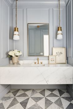 a bathroom with a marble counter top and gold fixtures on the mirror above it is a white vase with flowers