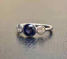 DeKara Designs Collection Beautiful Modern/Art Deco Ceylon Blue Sapphire and Diamond Ring Metal- 90% Platinum, 10% Iridium Stones- 1 Round Ceylon Blue Sapphire 1.00-1.05 Carats 6 MM, 2 Round Diamonds F-G VS2 Clarity, 0.40 Carats. Size-4-12 Classic and Timeless Art Deco Inspired Ceylon Blue Sapphire Diamond Three Stone Engagement Ring. There is a beautiful Ceylon Blue Sapphire that is extremely fiery and amazing in color that is featured as the center stone. The blue sapphire is professionally be Timeless Blue Round Diamond Ring, Blue Sapphire Ring In Platinum, Blue Sapphire Ring With Diamond And Polished Finish, Timeless Blue Rings With Polished Finish, Blue Sapphire Platinum Ring, Timeless Blue Sapphire Wedding Ring, Blue Three Stone Rings For Anniversary, Blue Diamond Ring With Polished Finish For Anniversary, Blue Three Stone Sapphire Ring