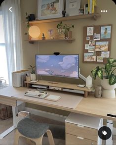 a desk with a computer on top of it and some plants in front of the monitor