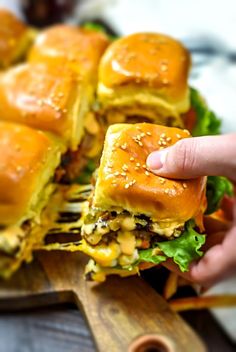 a person is holding a sandwich with cheese and lettuce on it as they sit on a cutting board