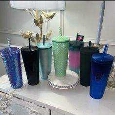 there are many different colored tumblers on the table with one drinking straw in it