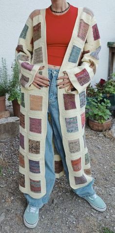 a woman standing in front of a white building wearing a sweater and jeans, with her hands on her hips