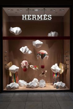 a window display with paper sculptures and lamps in it's glass case, which reads hermes