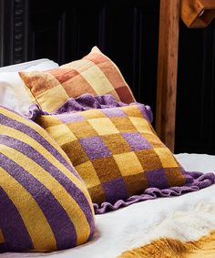 four different colored pillows sitting on top of a white bedspread next to a wooden headboard